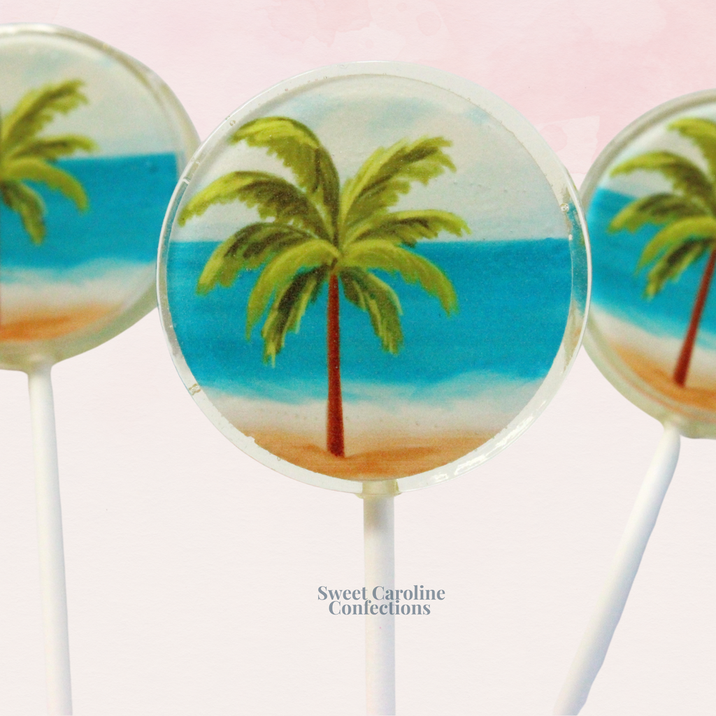 Handcrafted sparkle lollipop featuring a detailed palm tree design on a beach-themed background with edible glitter.
