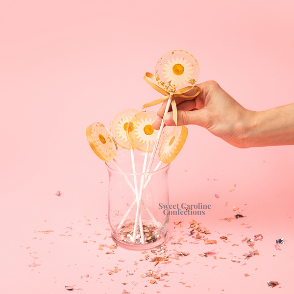 Classic white and yellow daisy flower lollipops with signature gold sparkle and hand-placed petals.