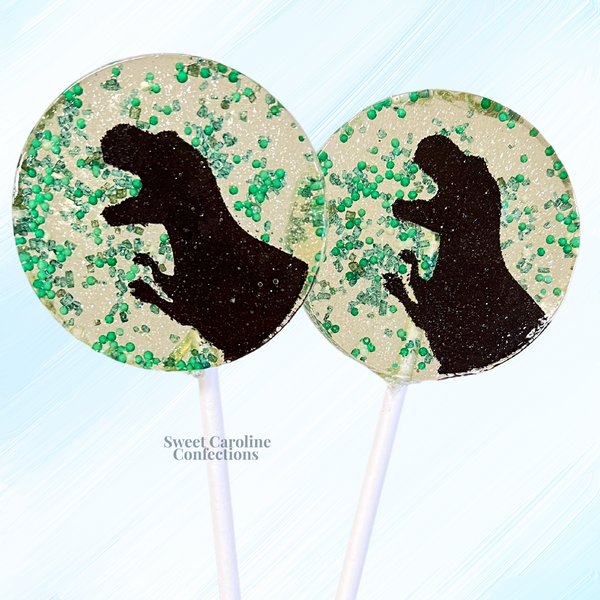 Handcrafted green and brown sparkle lollipops with various dinosaur designs, ideal for kids' prehistoric birthday parties.