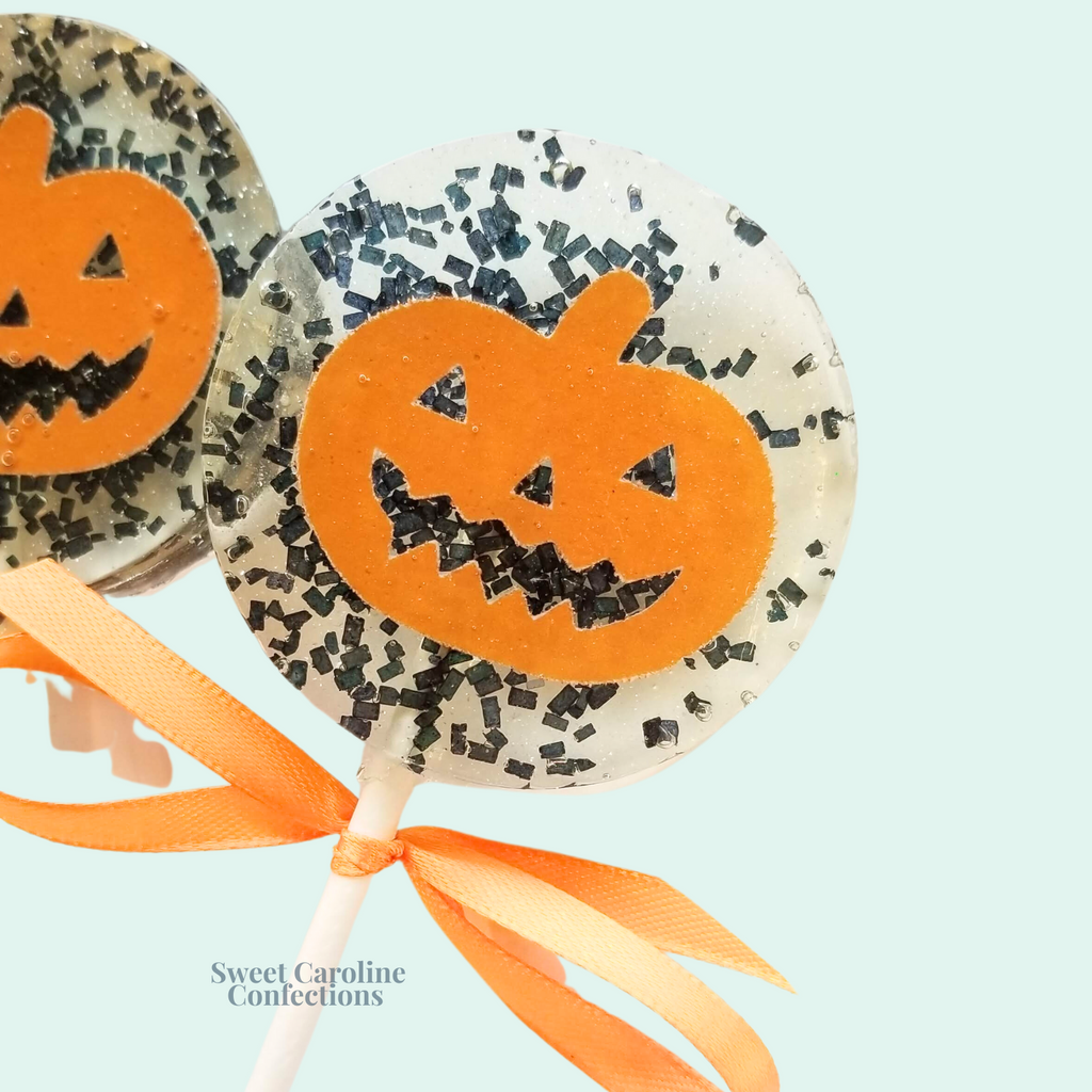 Orange and black jack-o’-lantern Halloween lollipops with intricate pumpkin cutouts and black sugar crystals from Sweet Caroline Confections.


