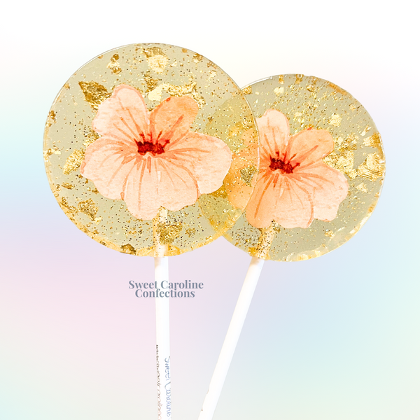 Delicate light peach flower lollipops featuring hand-placed edible petals and gold glitter accents.