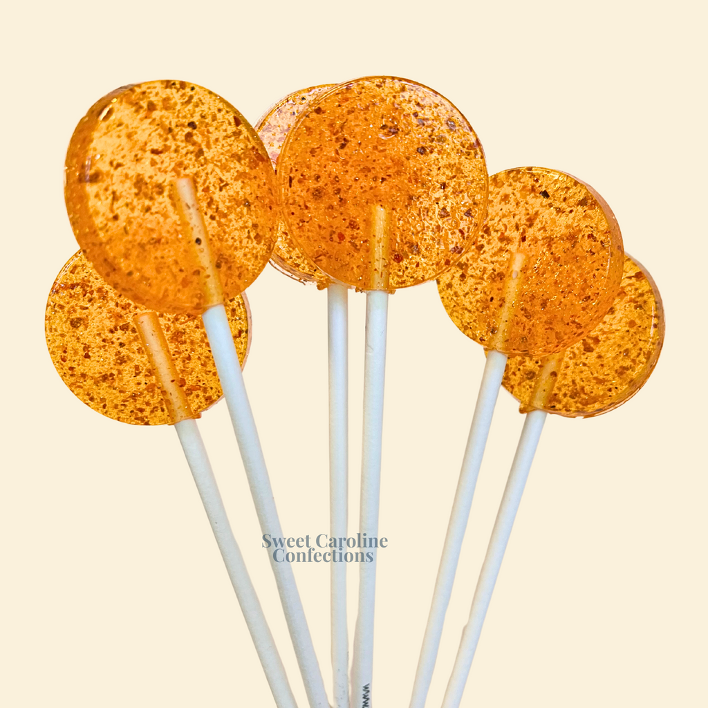 Mango flavored lollipops with a visible tajin spice swirl and fine edible sparkles.