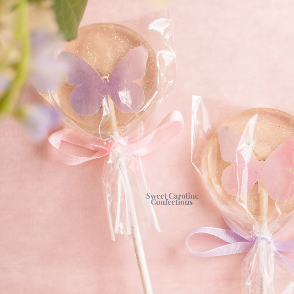 Light pink and lavender lollipops with edible butterfly designs and glitter.
