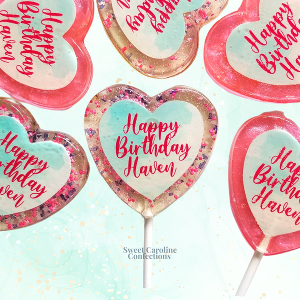 Vibrant hot pink and mint green lollipops with "Happy Birthday" text and edible sparkles, a fun treat for guests.