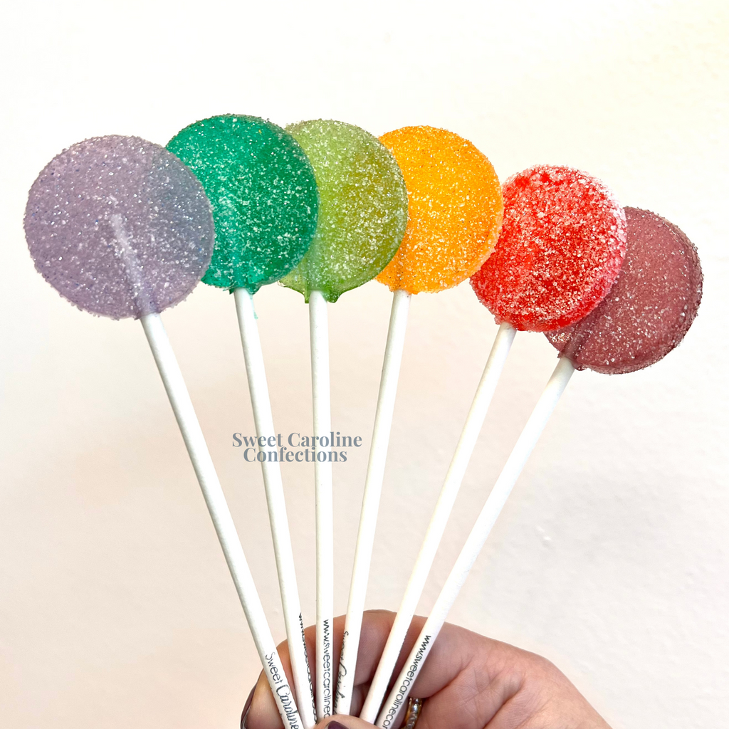 Clear sour sparkle lollipops with colorful edible glitter and a dusting of sour sugar crystals.